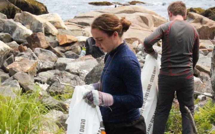 two teens pick up trash along a rocky shoreline during a service project with outward bound in maine